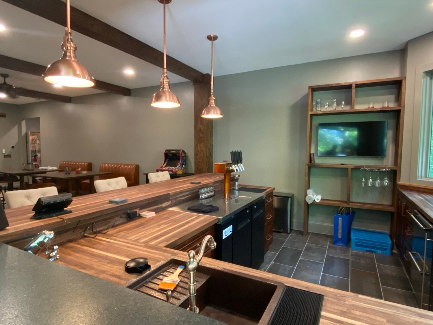 Basement wet bar in Alpharetta, GA with butcher block counters, copper pendant lights, an undermount sink, and tile flooring, Kohler Project by GHIR Construction