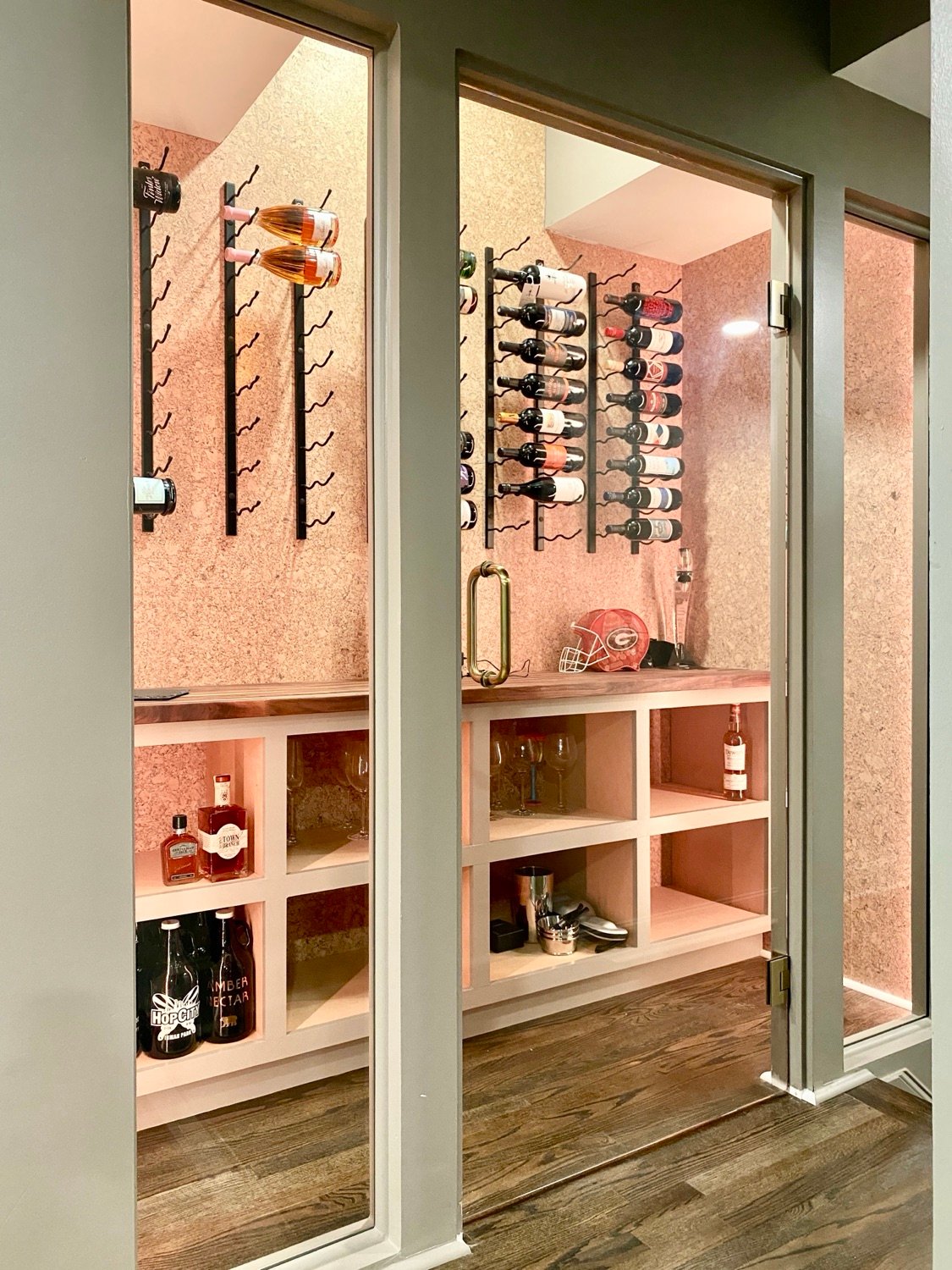 Glass-front basement wine room in Alpharetta, GA with wall-mounted bottle racks and built-in display shelving, Kohler Project by GHIR Construction
