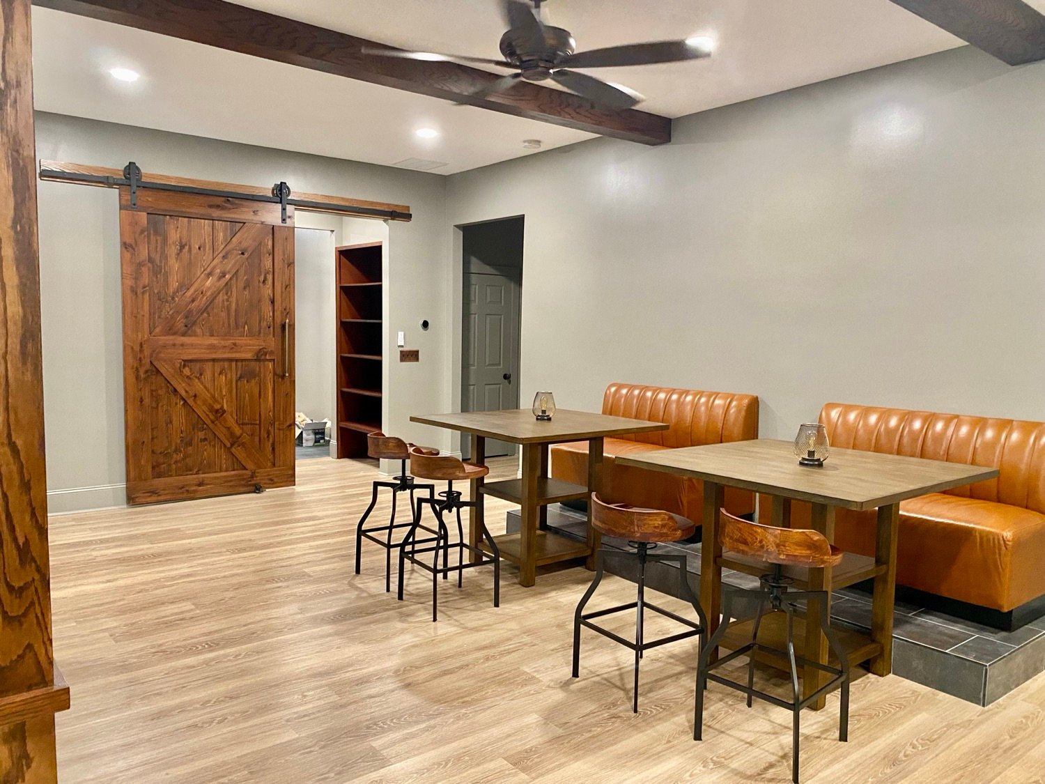 Finished basement lounge in Alpharetta, GA with leather banquette seating, bar tables, and a sliding barn door, Kohler Project by GHIR Construction